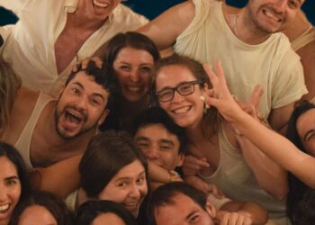 Grupo de personas sonrientes y abrazadas en un ambiente de celebración, vistiendo ropa cómoda y casual, disfrutando de la conexión y la energía compartida en un taller de biodanza